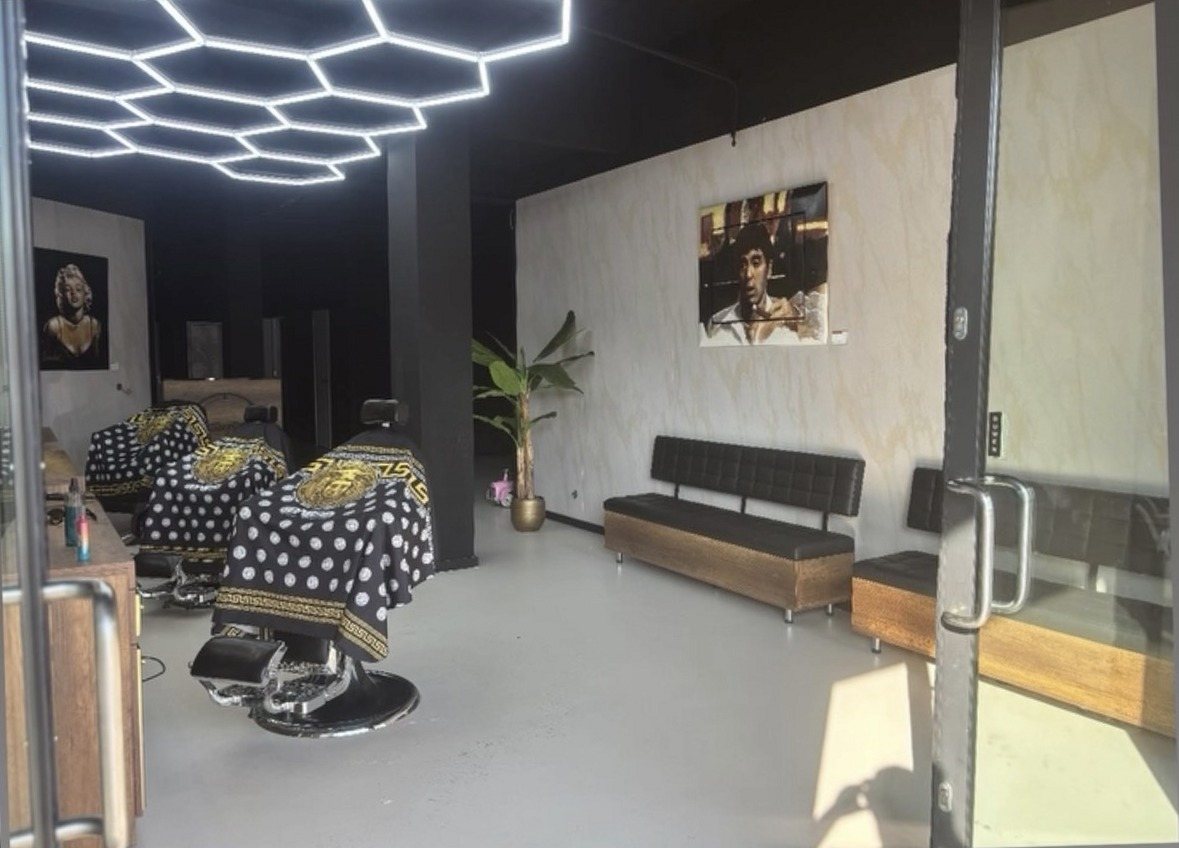 De zaak van binnen: twee kappersstoelen met zwart met gouden capes onder het zeshoekige plafondlicht